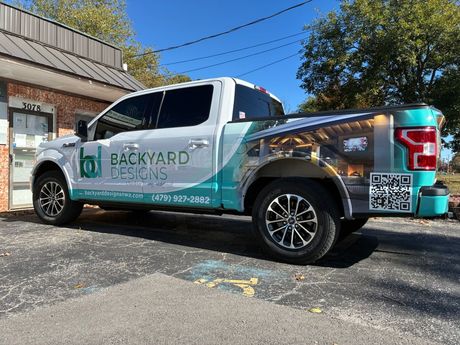 White pickup truck with turquoise and gray Backyard Escapes branding.