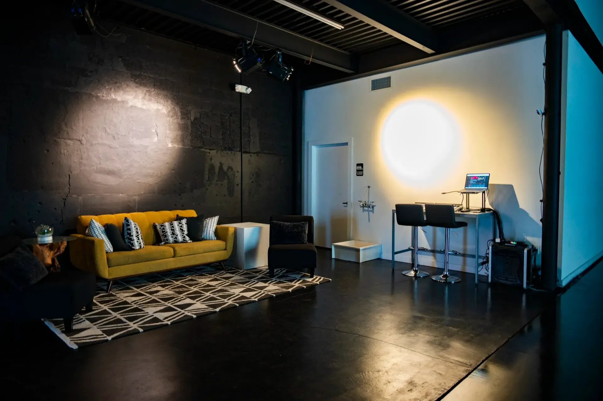 Studio with yellow couch, black and white rug, and bright circle light on white wall.