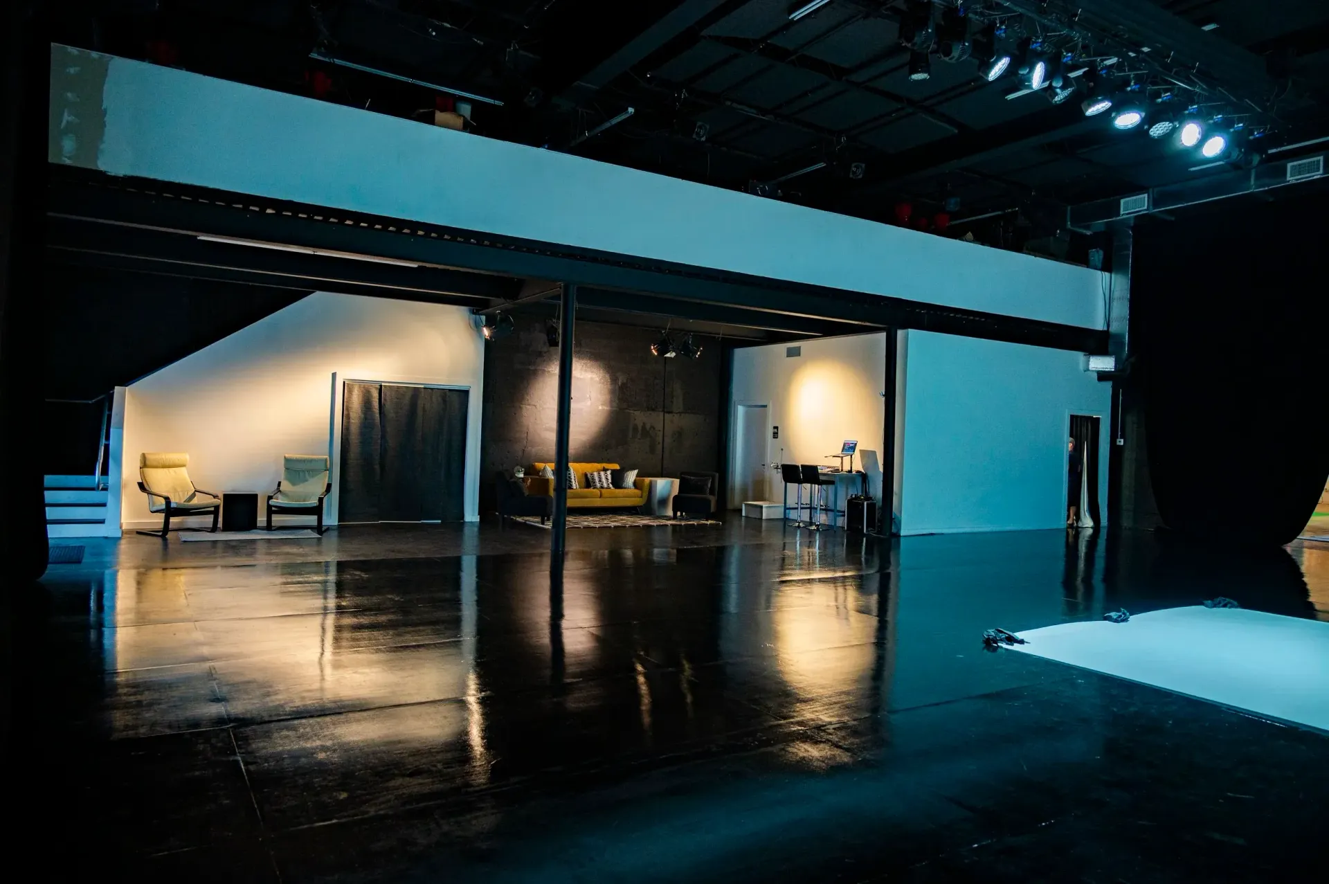 Empty studio with glossy black floor reflecting lights, couches, and white walls.