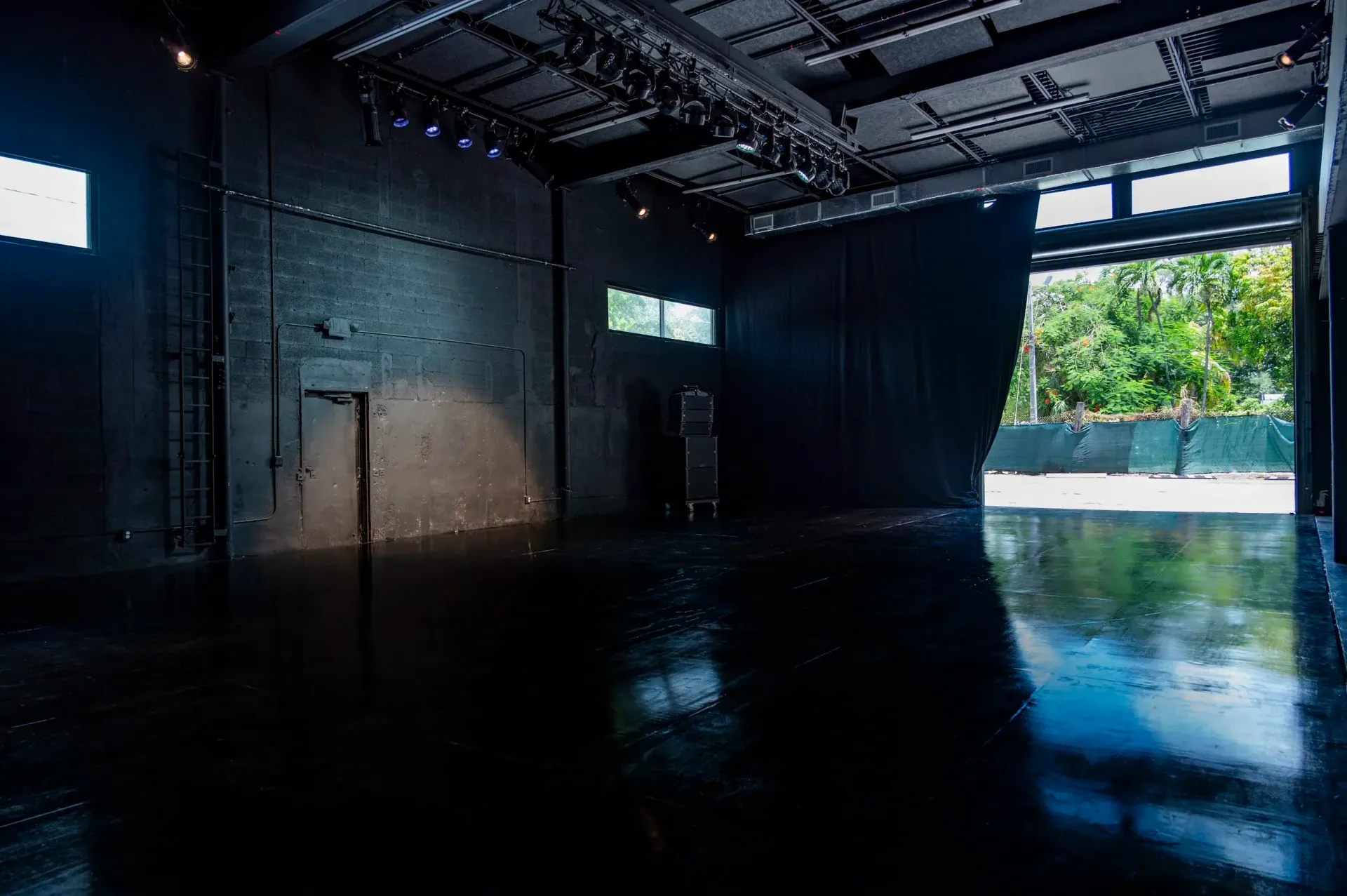 Dark room with open doorway to outside greenery and wet, shiny floor.