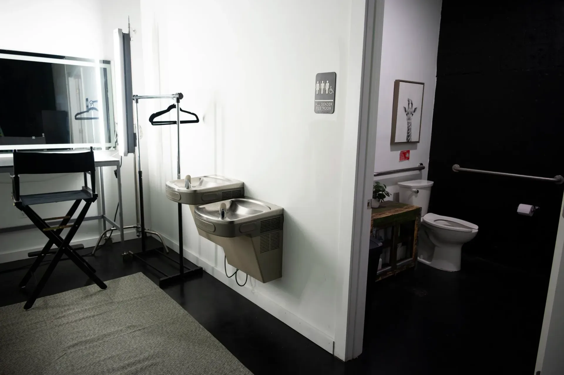A dressing room with a sink and mirror on a white wall, and a toilet in the corner.