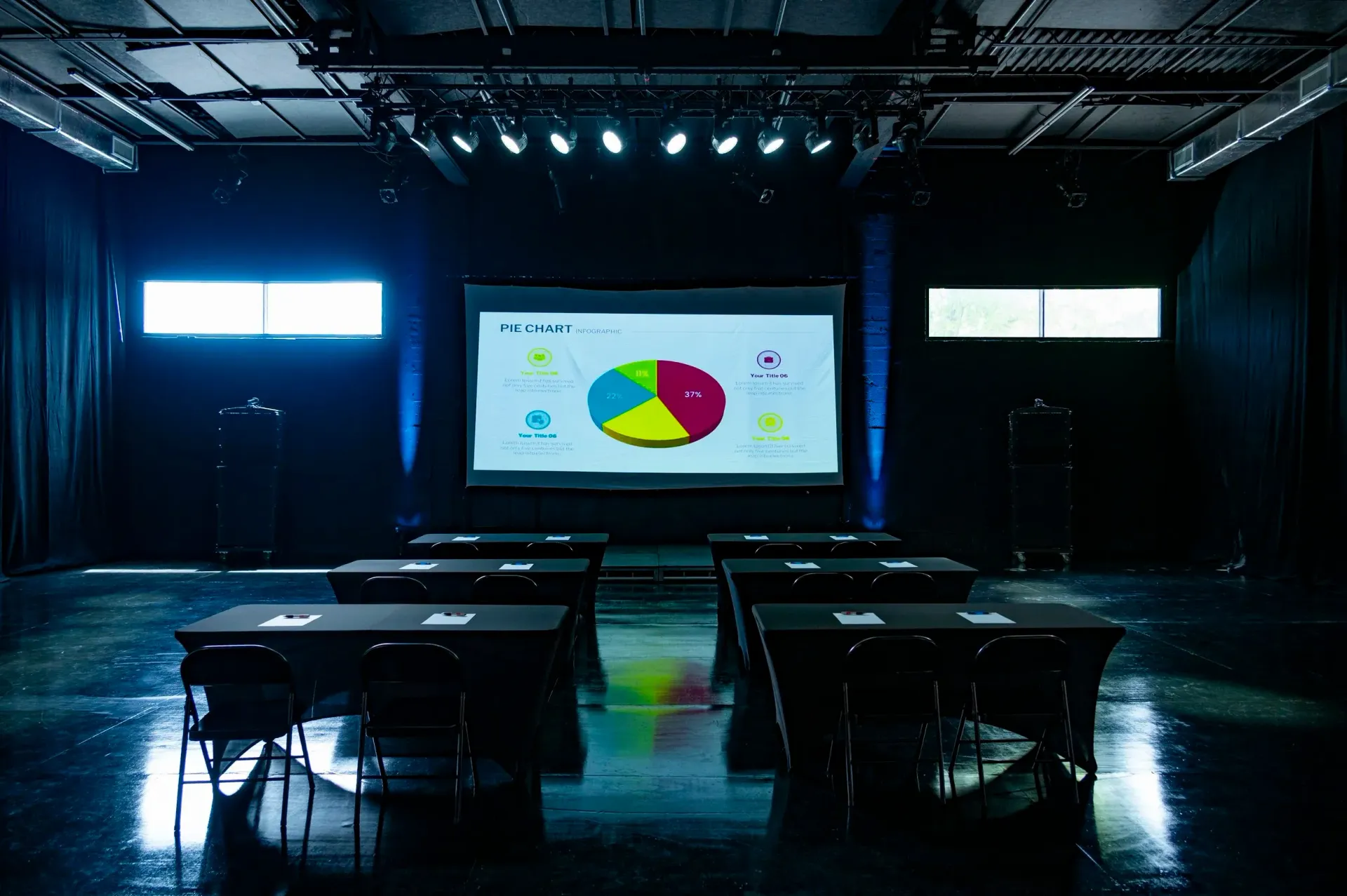 Conference room with tables, projector screen showing a pie chart, and stage lighting.
