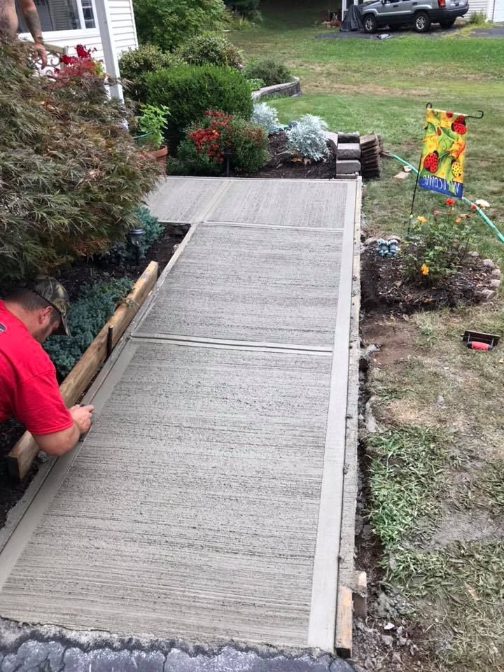 A man is working on a concrete walkway in front of a house.