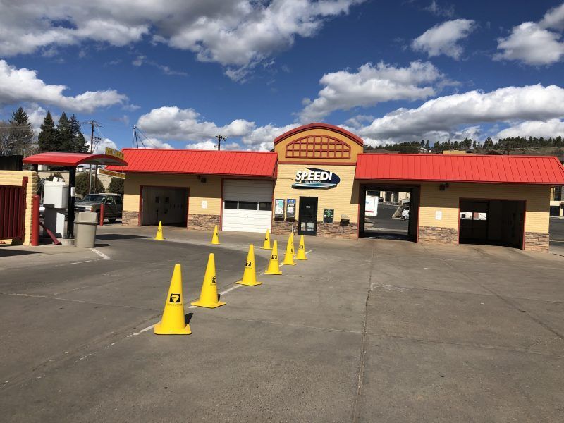 Car wash with red roof, beige walls, and yellow cones guiding traffic under a blue sky.