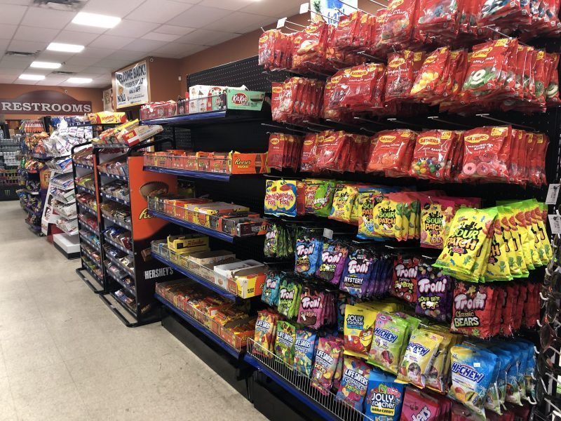 Shelves in a convenience store filled with various candy and snacks, a restroom sign is visible.