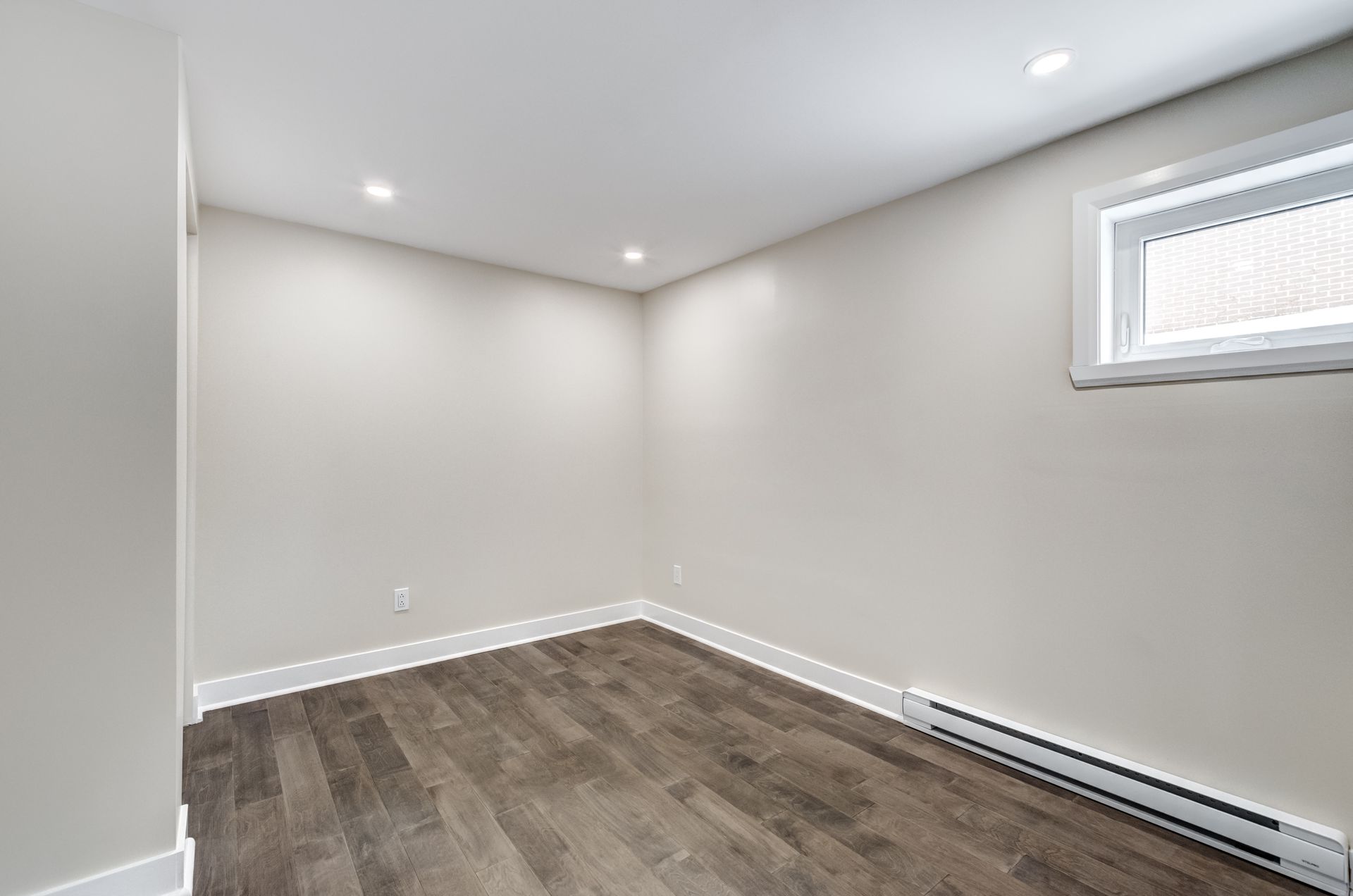 Empty gray room with recessed lights, dark wood floor, and a small window