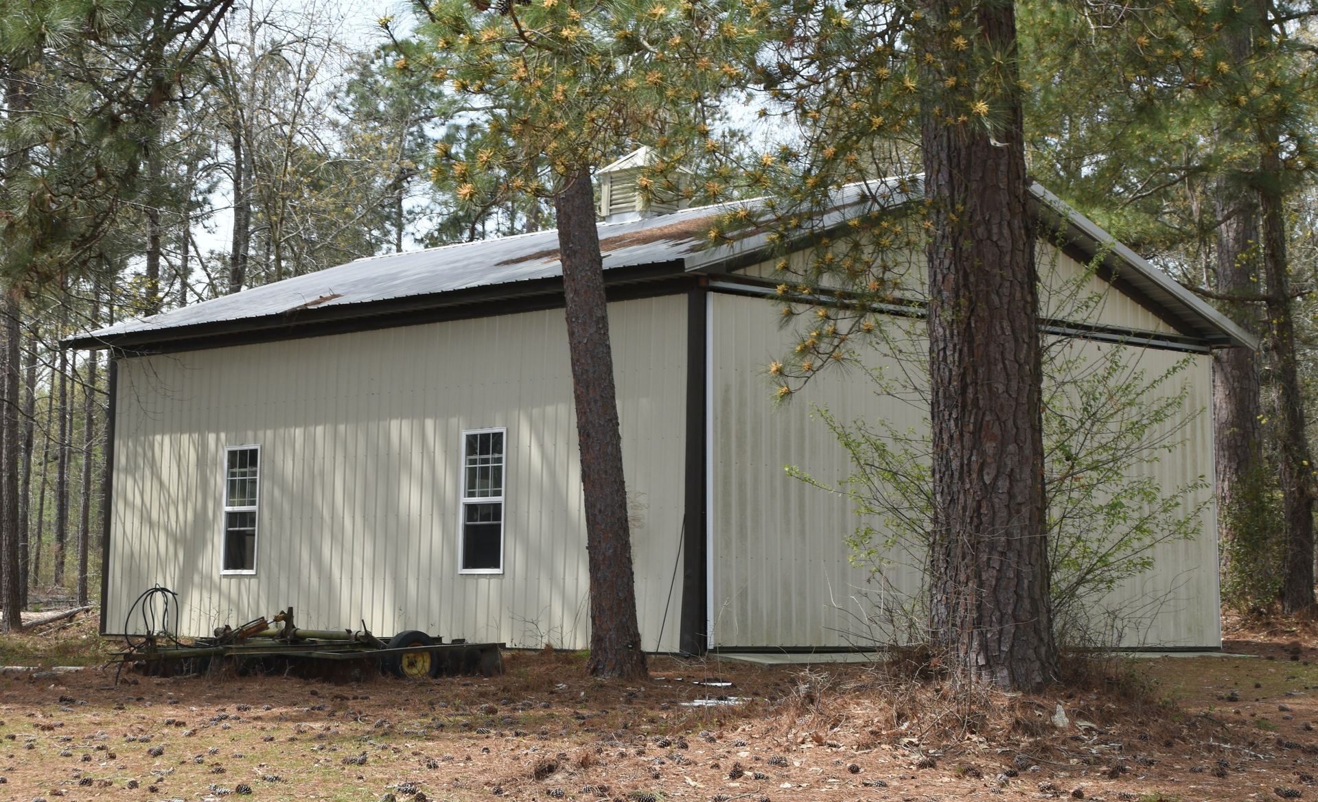White metal building in a wooded area, with a low roof and several windows.