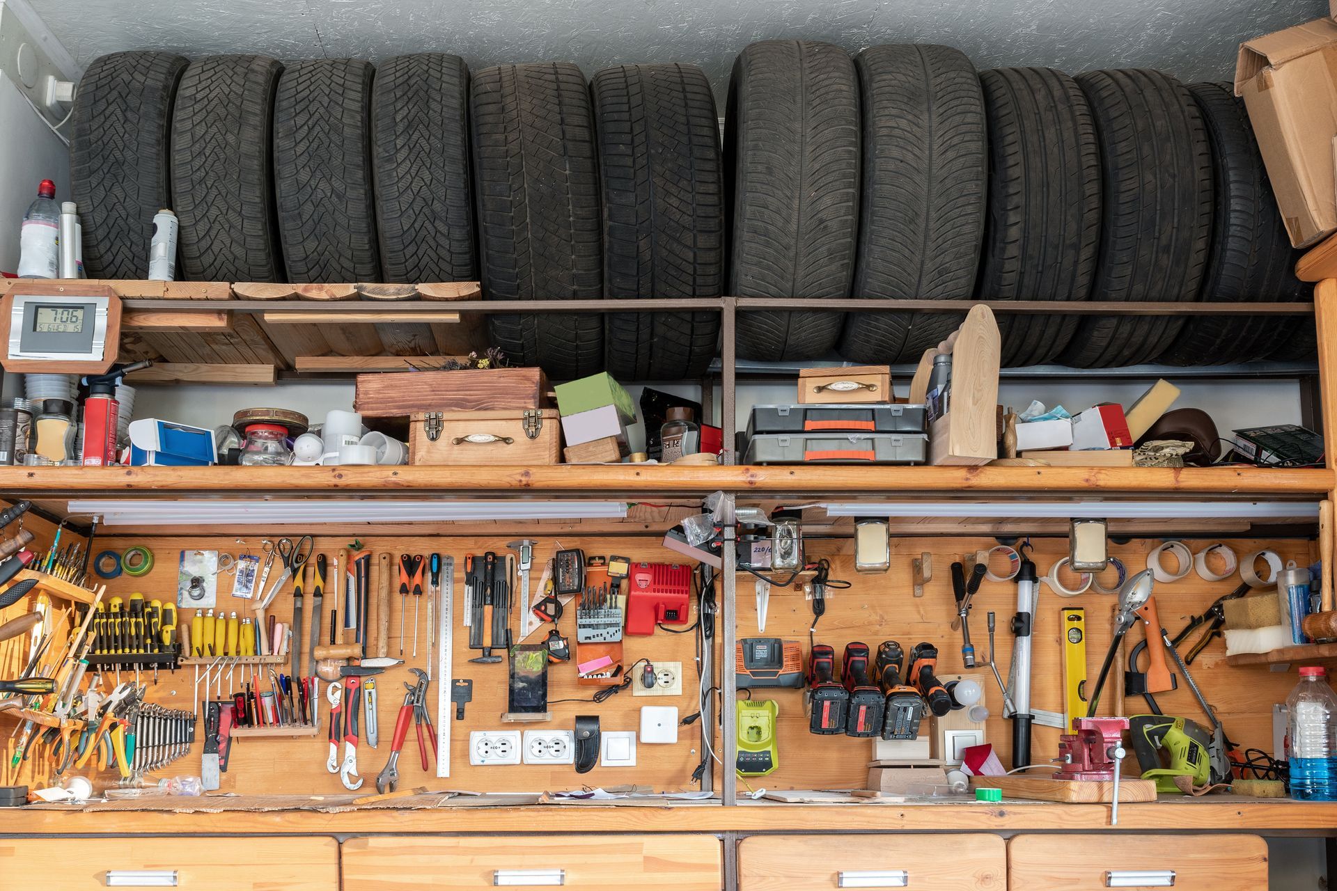 Organized garage workbench with tools, supplies, and stacked tires on shelves above
