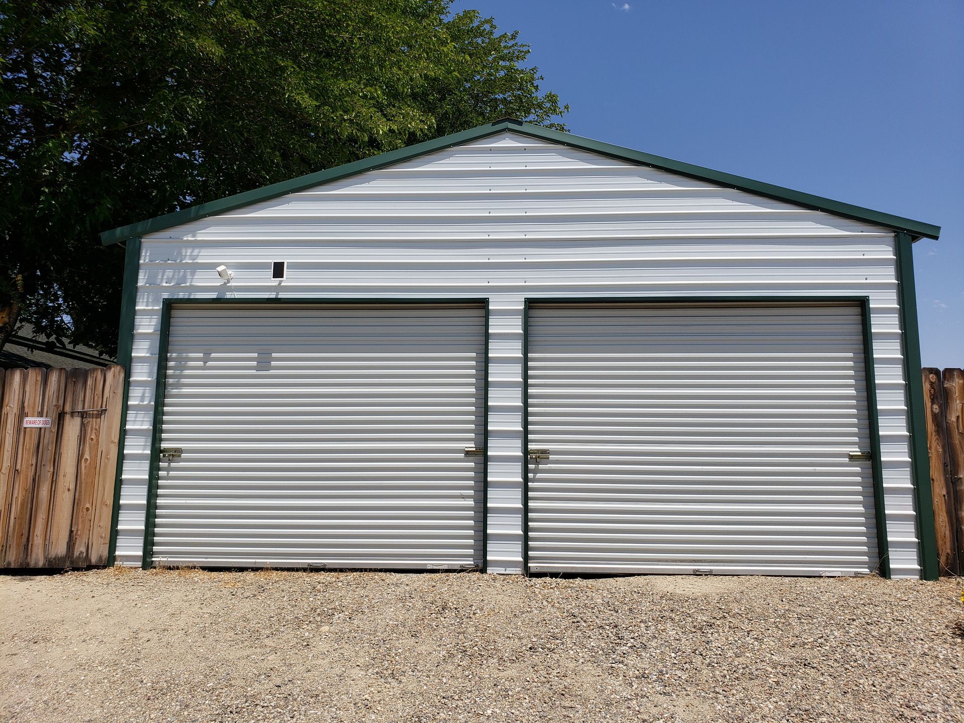White metal garage with two closed gray doors and gravel driveway under trees