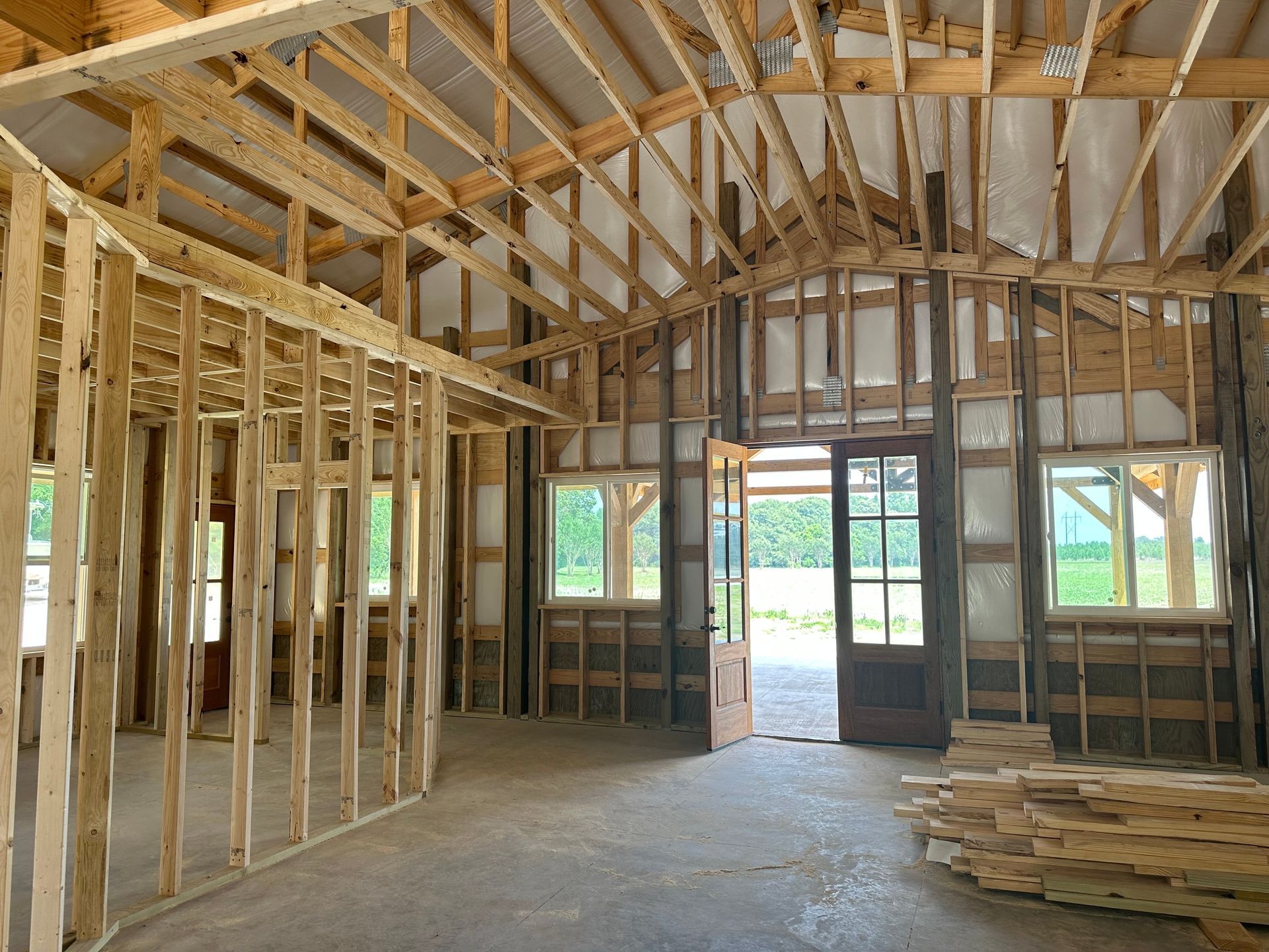 Interior of an unfinished wooden house frame with exposed studs, rafters, and stacks of lumber on the floor.