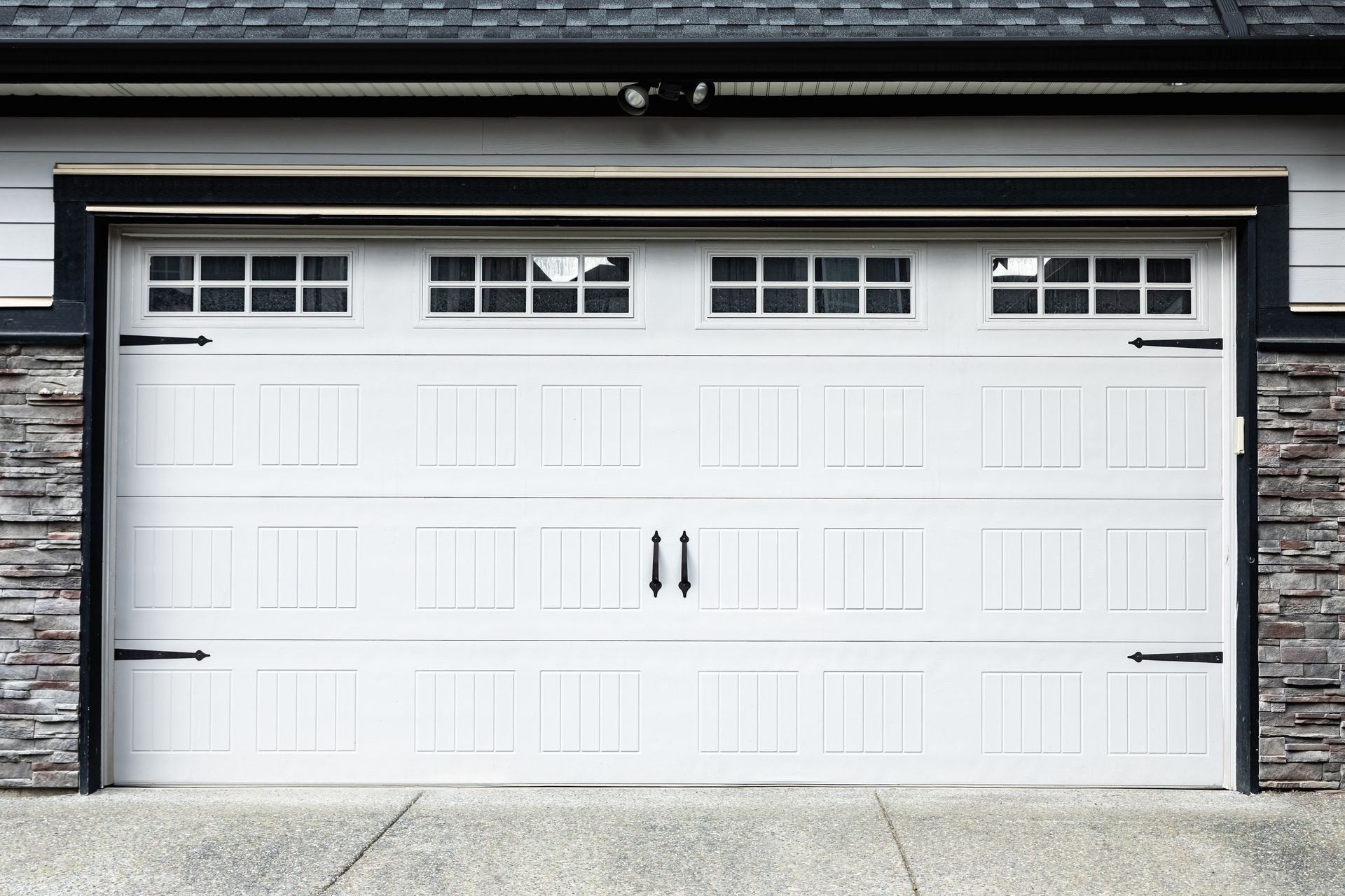 White double garage door with small windows and black handles on a stone house exterior