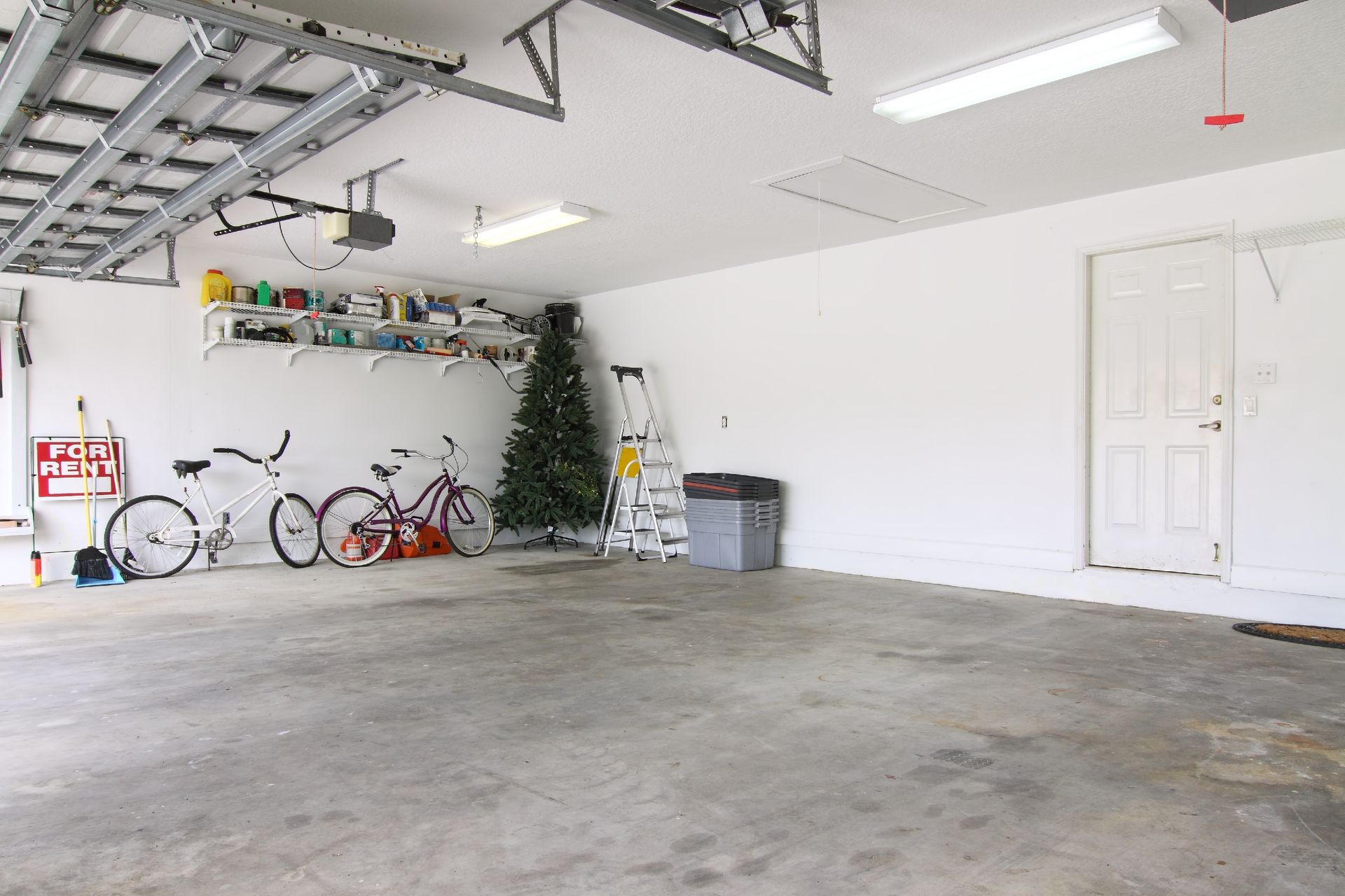 Empty garage with concrete floor, bicycles on the left, and white walls with a door on the right