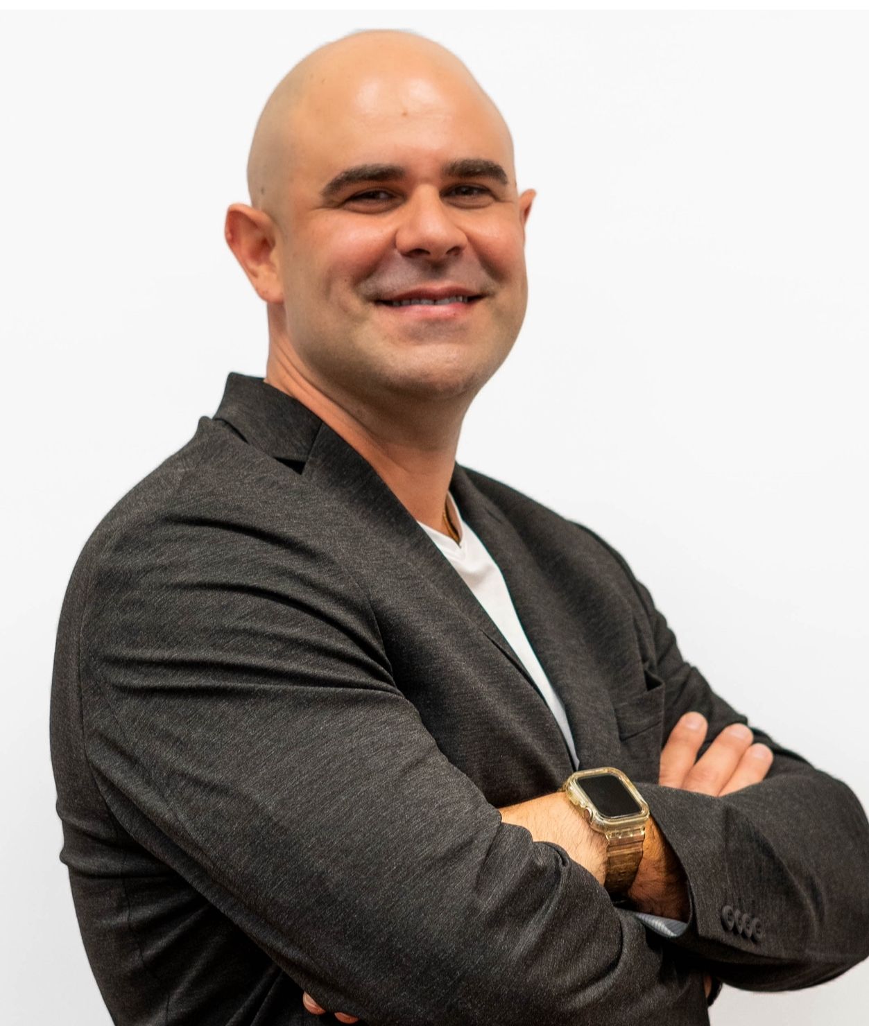A bald man in a suit is smiling with his arms crossed