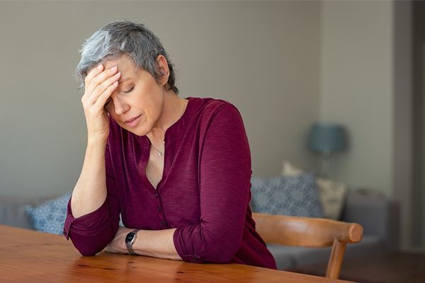 a woman is sitting at a table with her hand on her forehead .