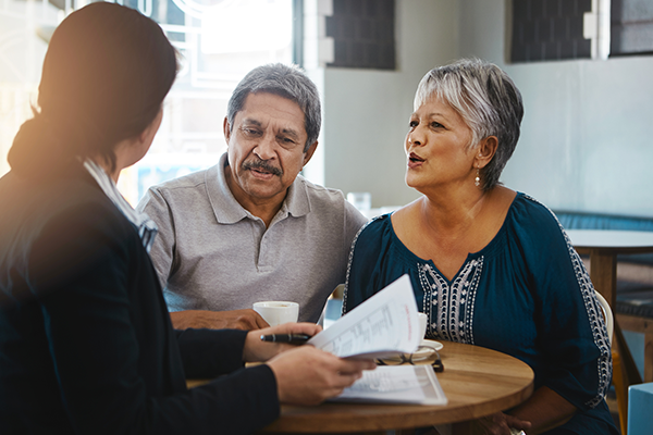 an elderly couple is sitting at a table talking to a woman .