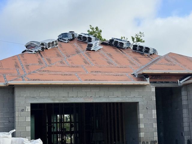 Bundles of roof shingles sitting on the underlayment of a residential home under construction.
