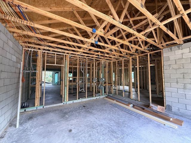 An interior view of a residential construction site featuring concrete block walls and wooden wall and ceiling framing.