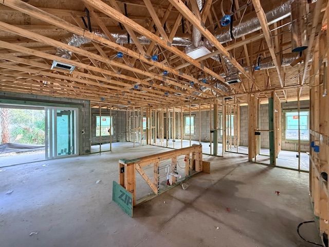 Interior of a house under construction with exposed wooden framing, concrete flooring, and suspended HVAC ductwork.