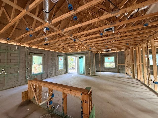 Unfinished house interior with exposed wooden roof trusses, cinder block walls, and windows.