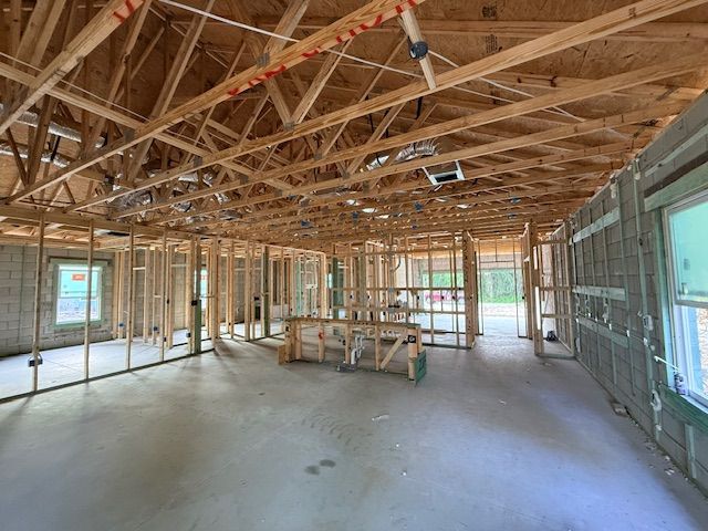 Interior view of a residential building under construction with exposed wooden framing and concrete flooring.