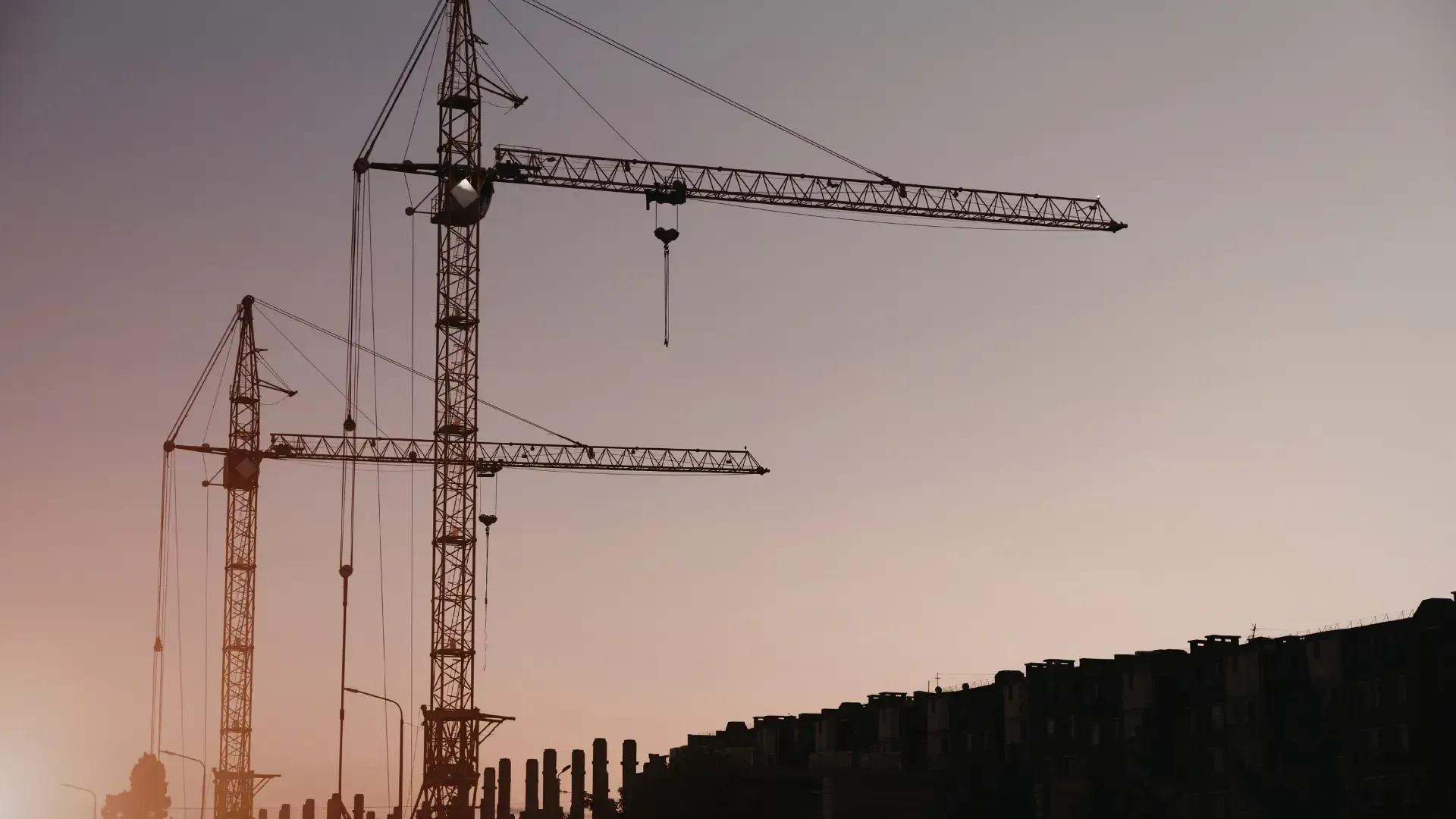 Construction cranes silhouetted against a dusky, gradient sky.