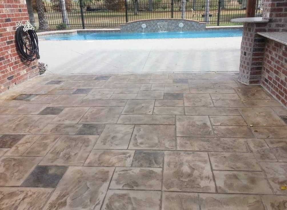 A patio with a brick wall and a swimming pool in the background.