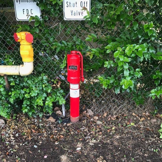 A red fire hydrant is sitting next to a chain link fence.