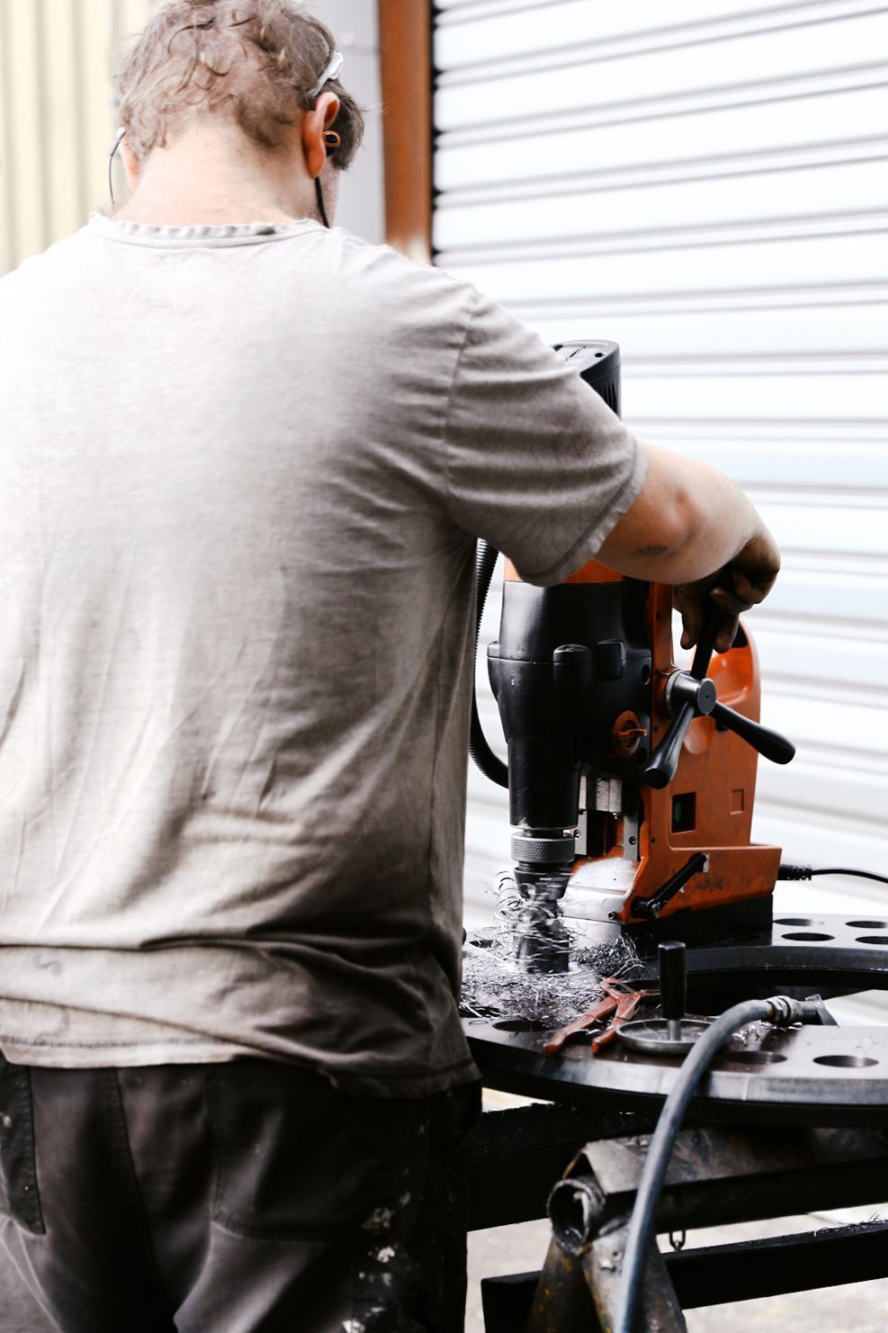 A person operating a magnetic drill on a metal plate in a workshop. A person operating a magnetic drill on a metal plate in a workshop.