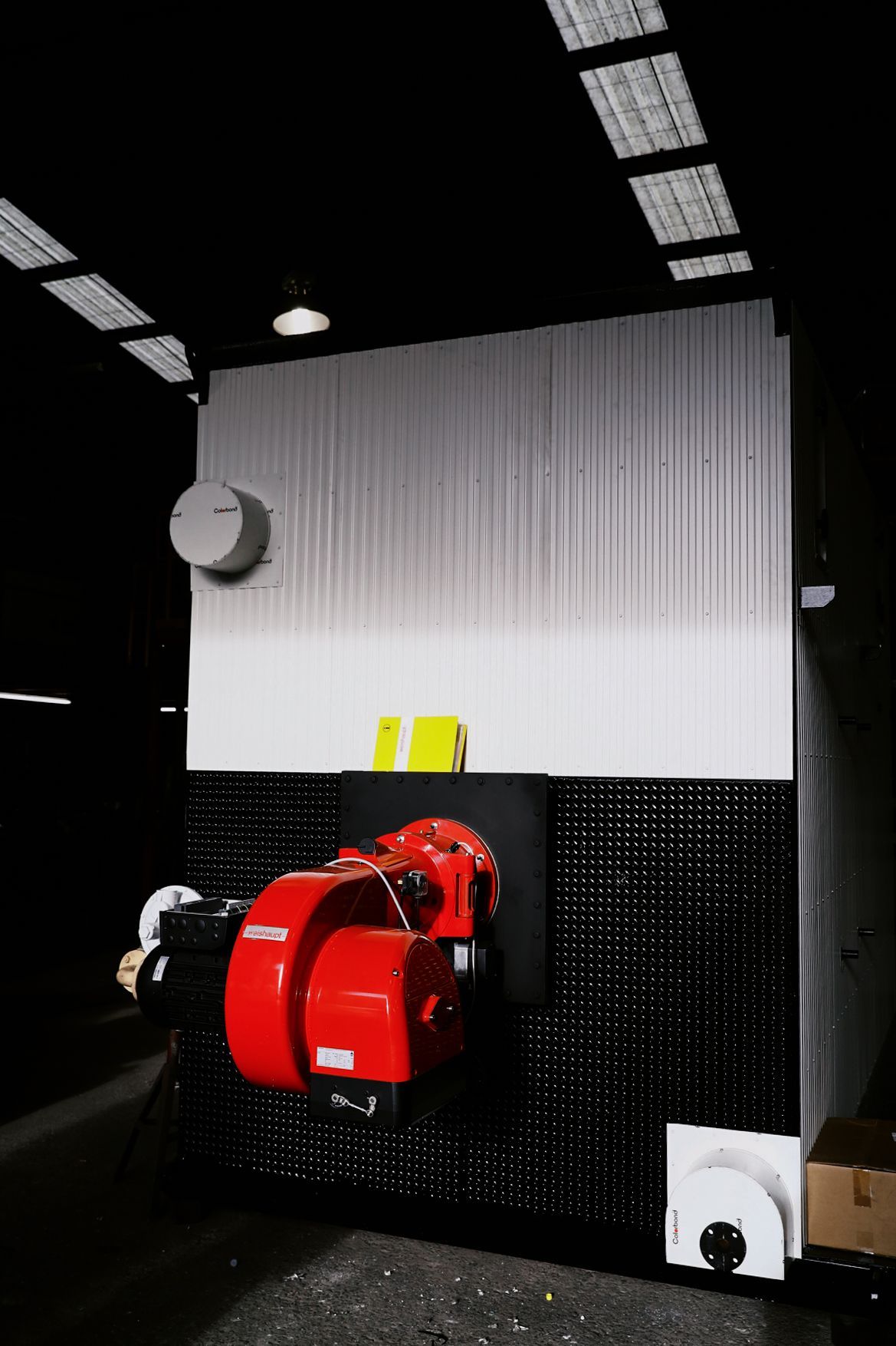 A large, industrial boiler unit with a prominent, bright red burner attached to its black and white metal housing.