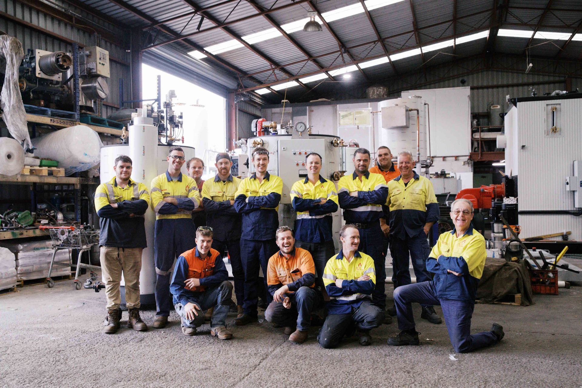 A group of people wearing high-visibility work uniforms smile while posing in an industrial workshop.