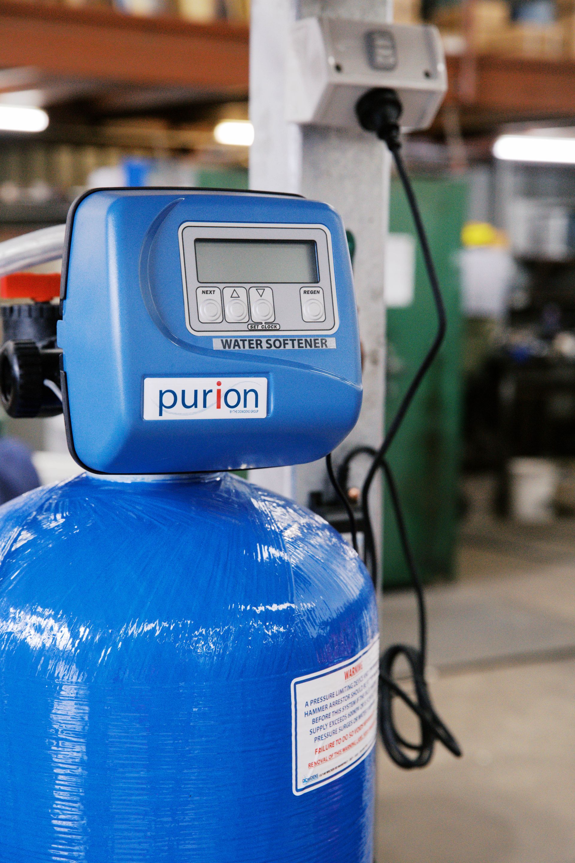 A blue Purion water filtration system tank with a digital control head plugged into an electrical outlet.