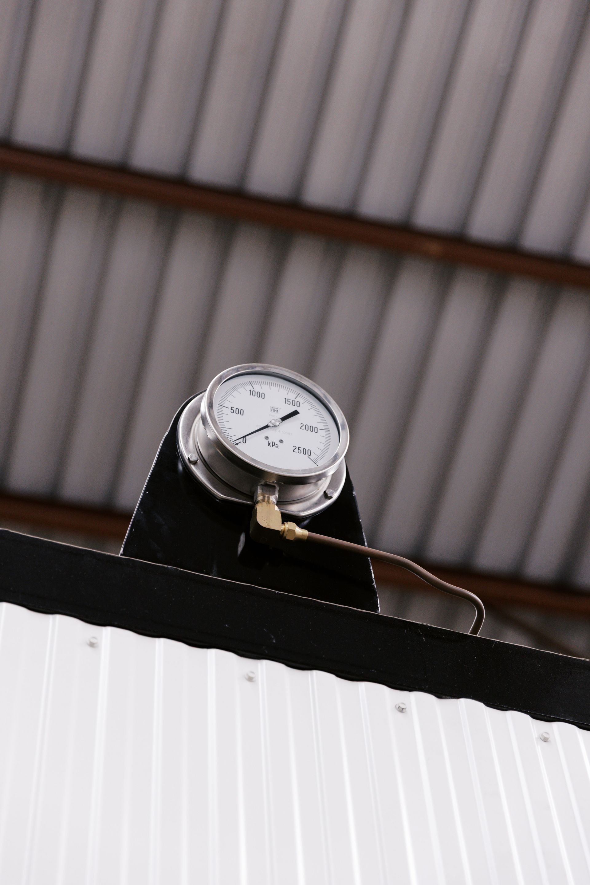 A round analog pressure gauge mounted atop a white, corrugated metal structure beneath a slatted ceiling.