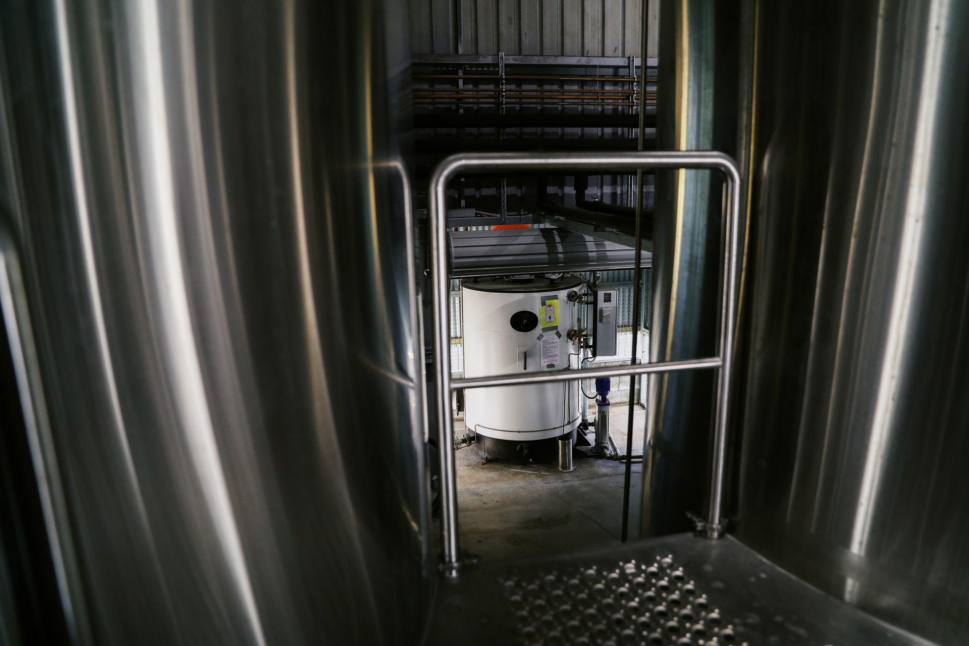 A metal platform with a safety railing looks down into a room containing a white industrial tank.