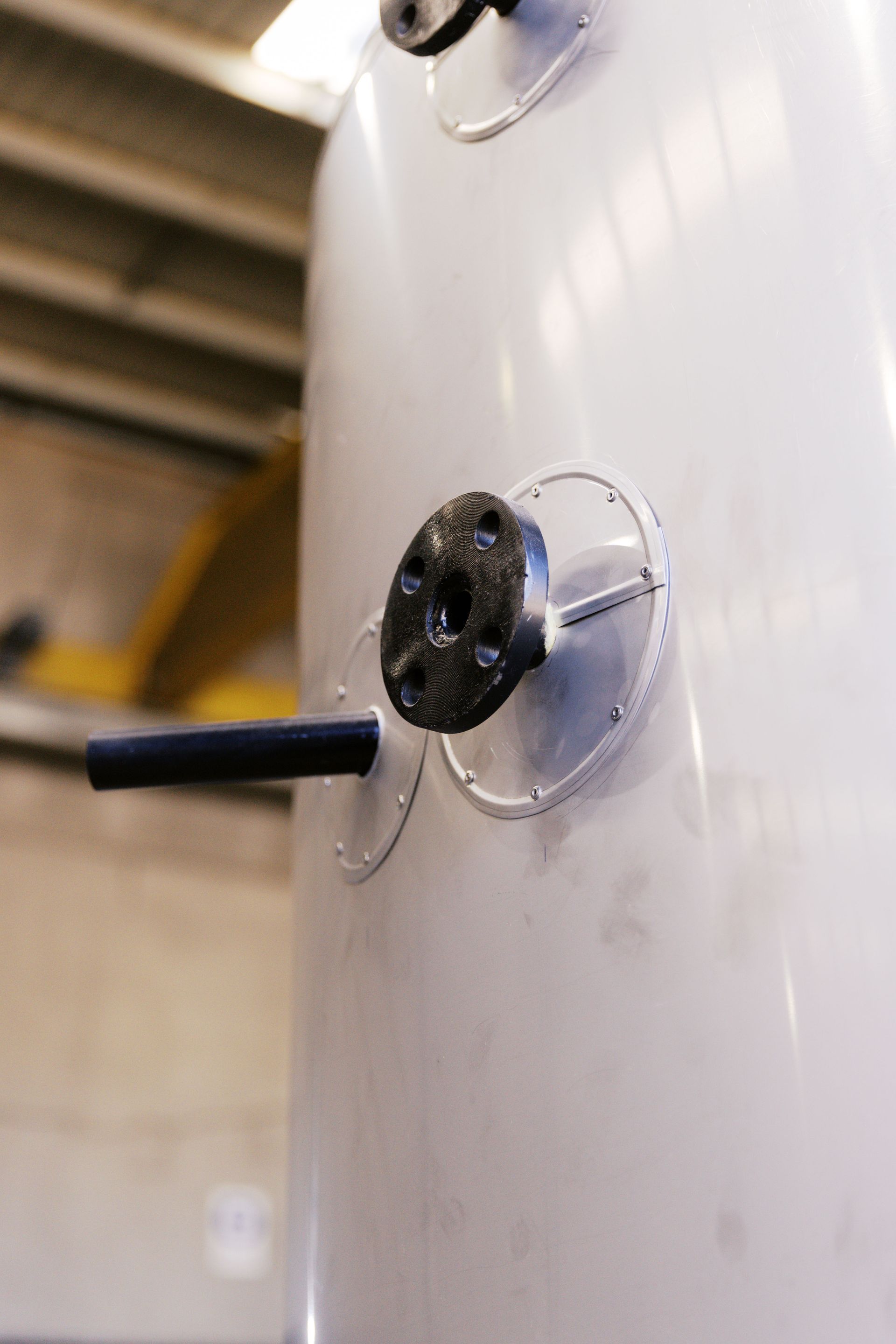 A large white industrial tank with a circular black pipe flange and an attached horizontal pipe protruding from its side.