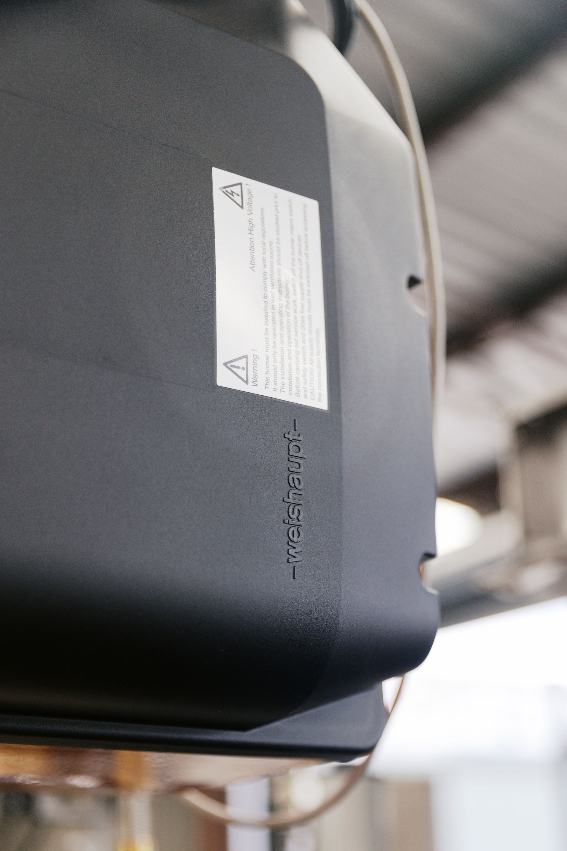 A close-up of a black garage door opener mounted to a ceiling with a white warning label attached to its side.