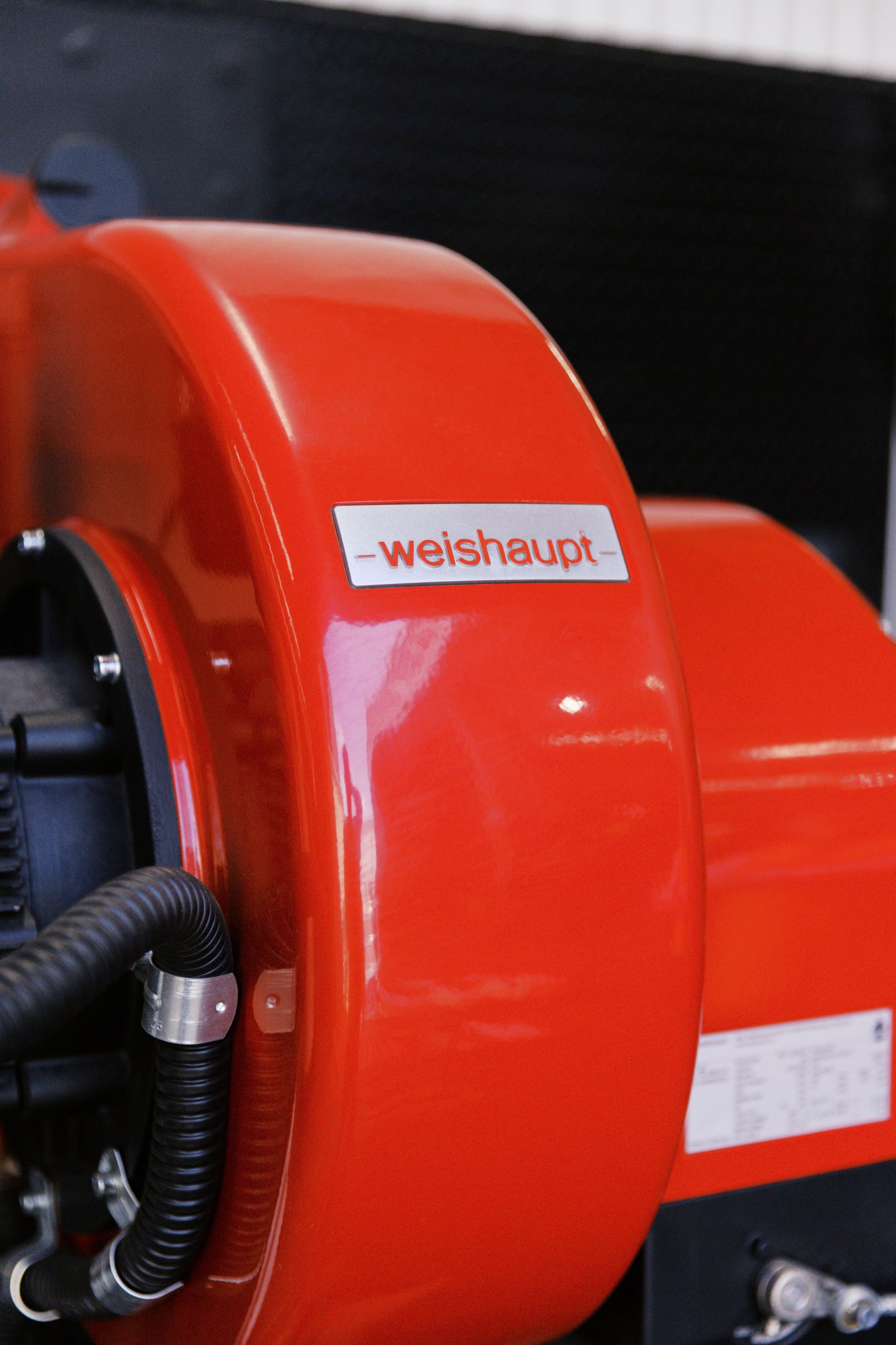 A bright red industrial burner or fan unit with a metallic Weishaupt brand label attached to the side.