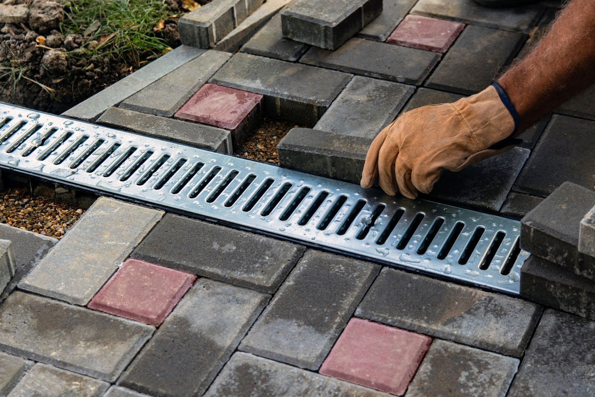 Installing a drainage grate in a brick patio. A gloved hand places a brick.