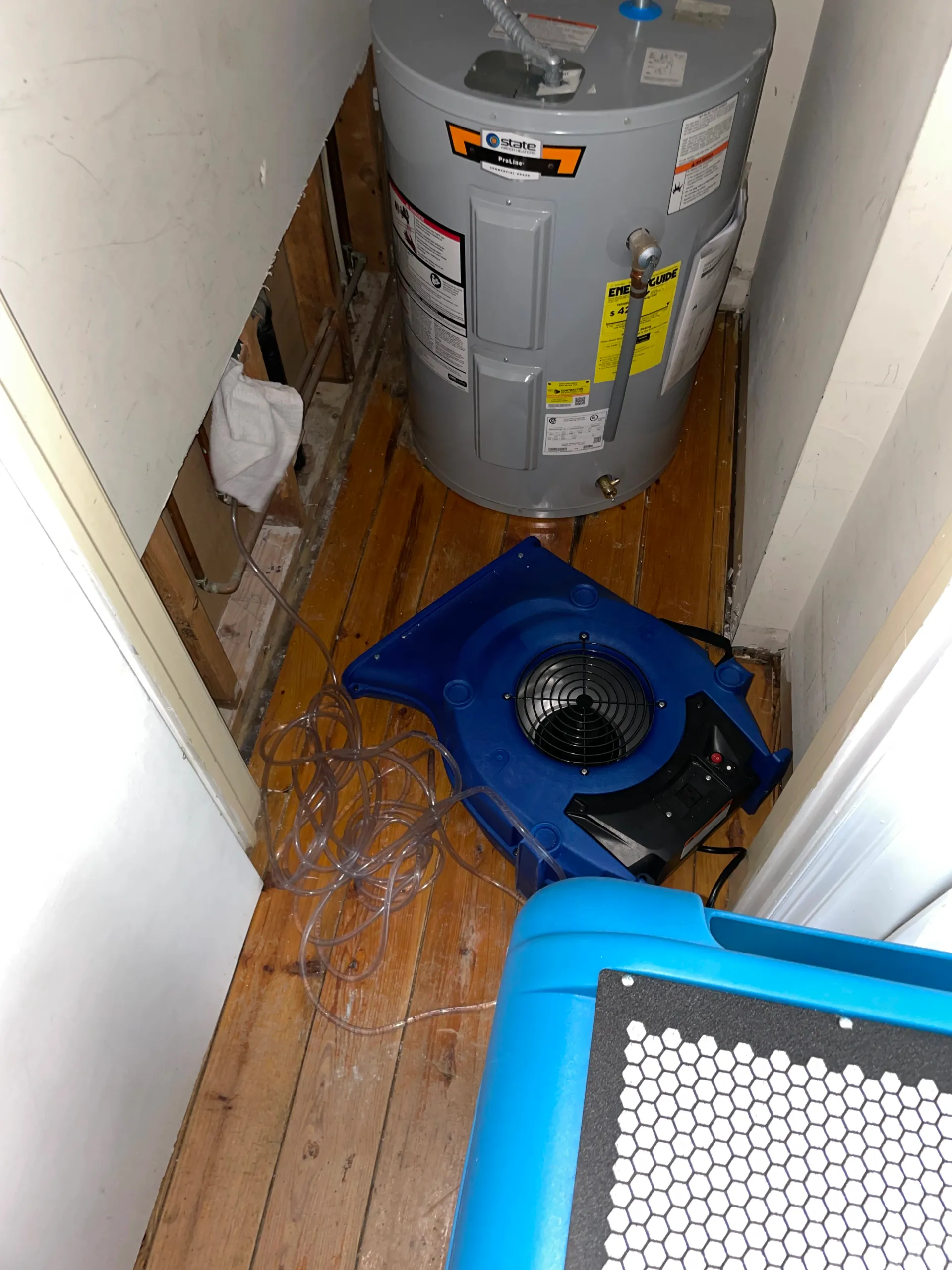 a water heater is sitting on a wooden floor next to a fan .