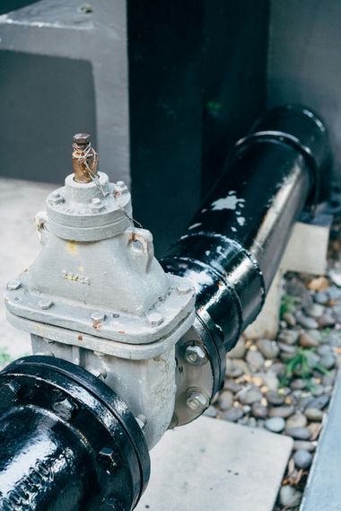 Black pipeline with a gray fire hydrant valve beside a concrete wall and gravel ground