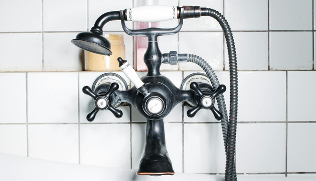 Black vintage bathroom sink faucet with flexible shower hose against white tiled wall