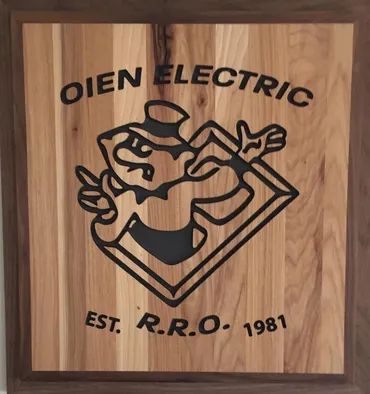 A wooden plaque for Oien Electric (est. 1981) featuring a black-engraved logo of a cartoon figure in a top hat.