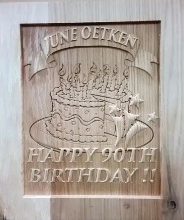 A wood carving featuring a birthday cake with candles, decorative stars, and text reading