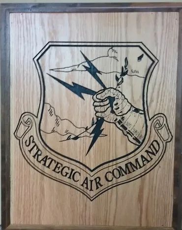 A wooden plaque featuring the engraved black-ink emblem of the U.S. Air Force Strategic Air Command.
