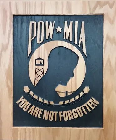 Wood cutout of the POW/MIA emblem featuring a soldier's silhouette, a guard tower, and the text