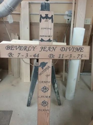 A memorial wooden cross for Beverly Jean Divine, listing her birth and death dates, with names inscribed below.