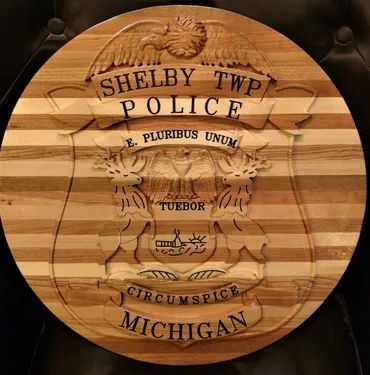 A wooden circular plaque featuring the Shelby Township Police badge design with the Michigan state seal.