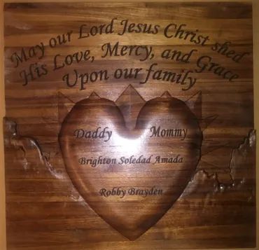 A wood-carved plaque with a central heart, engraved with a prayer and the family names: Daddy, Mommy, Brighton, and Robby.