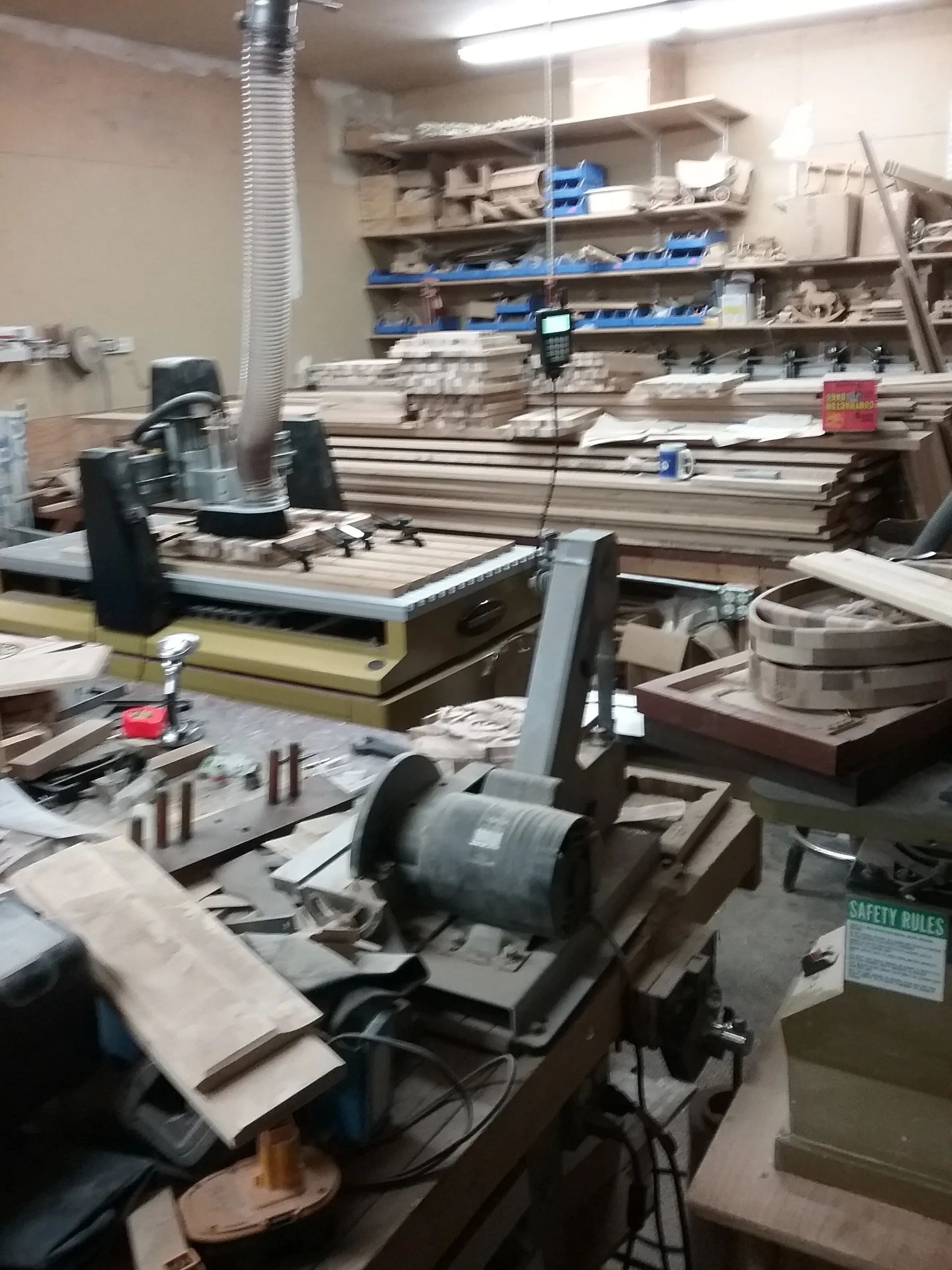 A woodworking shop featuring a CNC machine, various tools, and stacks of lumber on shelves in the background.