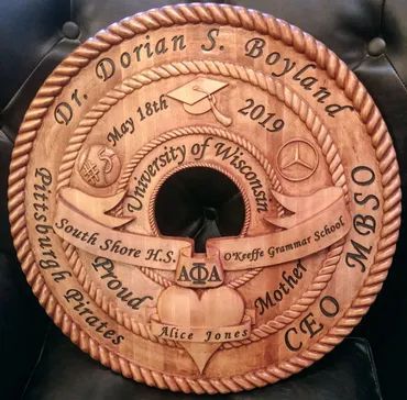 A circular, wooden engraved plaque commemorating Dr. Dorian S. Boyland, listing his education, career, and family roots.