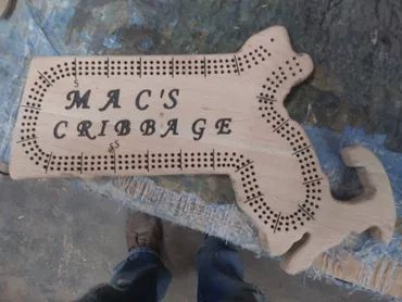A handmade wooden cribbage board shaped like the state of Massachusetts, inscribed with